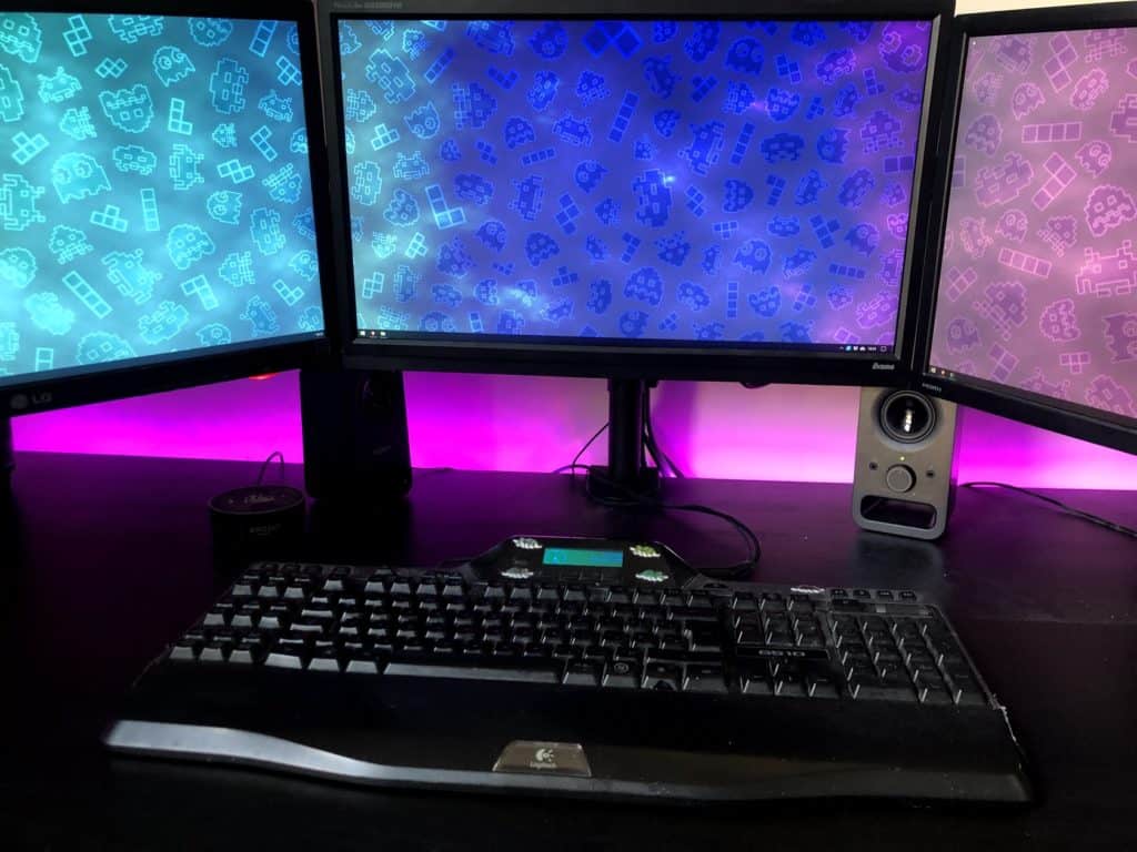 Computer desk setup with 3 monitors and LED strip lights behind it.