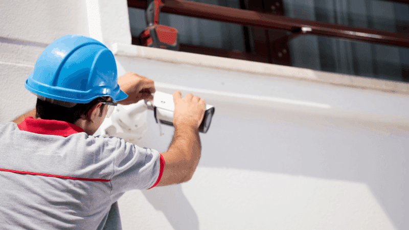 Man with helmet installing a security camera outside.