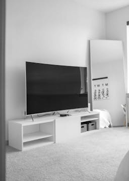 tv on a white tv shelf with white walls and mirror on wall