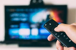 person holding amazon firestick remote with tv in background