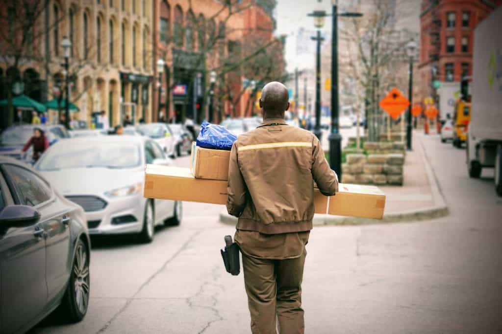 Delivery man carrying large packages walking outside.