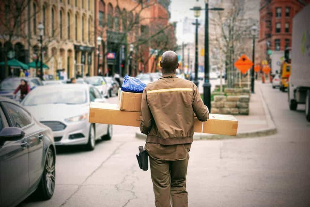Delivery man carrying large packages walking outside.