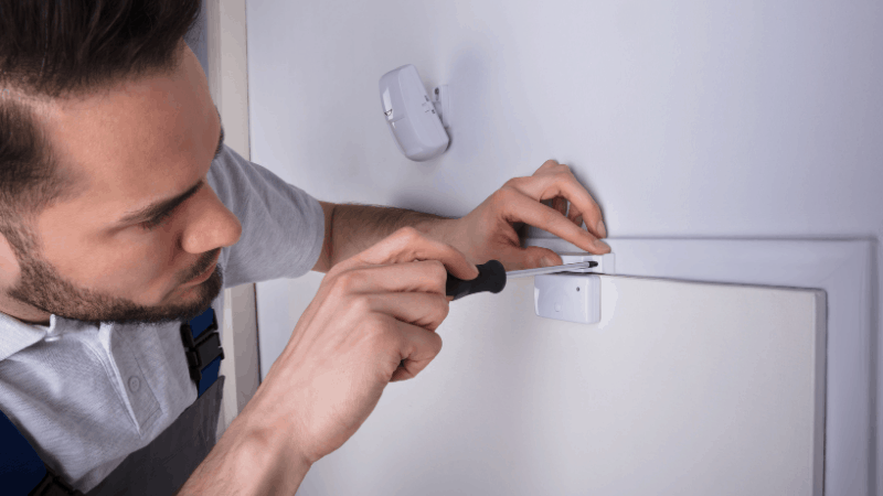 Man installing a smart door sensor for alarm system.
