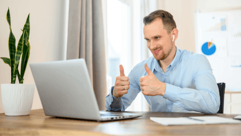 Happy man with airpods on with thumbs up on a laptop.