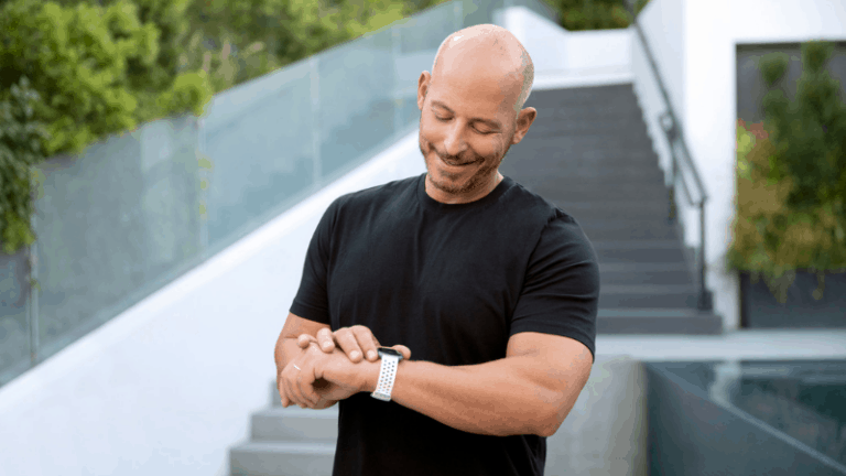 Man smiling at fitbit watch while outside working out.