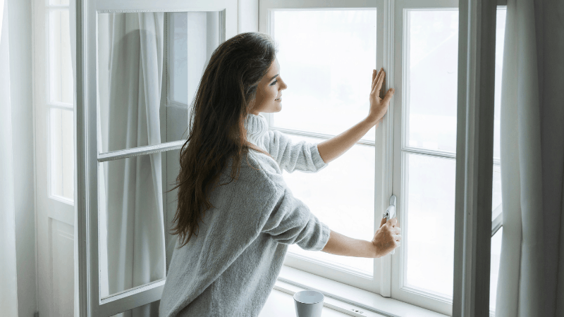 Woman smiling looking outside window while opening window.
