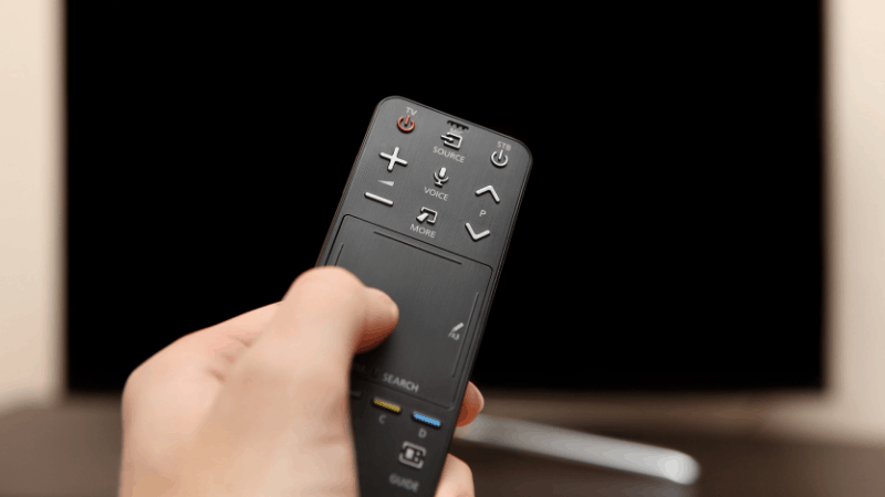 Hand pressing universal remote pointing to a TV that is powered off.