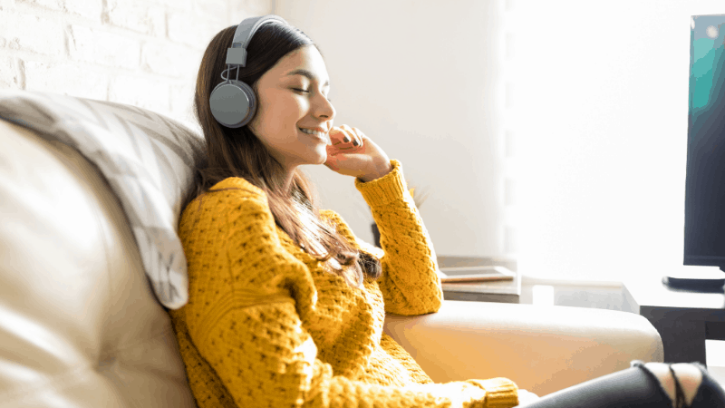Girl wearing yellow sweater enjoying listening to music with headphones.