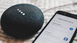 Black Google nest mini speaker on bed with smartphone
