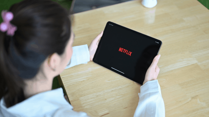 person holding an ipad with netflix open on a bamboo counter