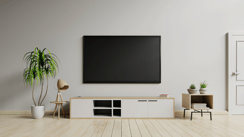 Smart TV mounted to wall in a living room with lamp, plants, and shelf.