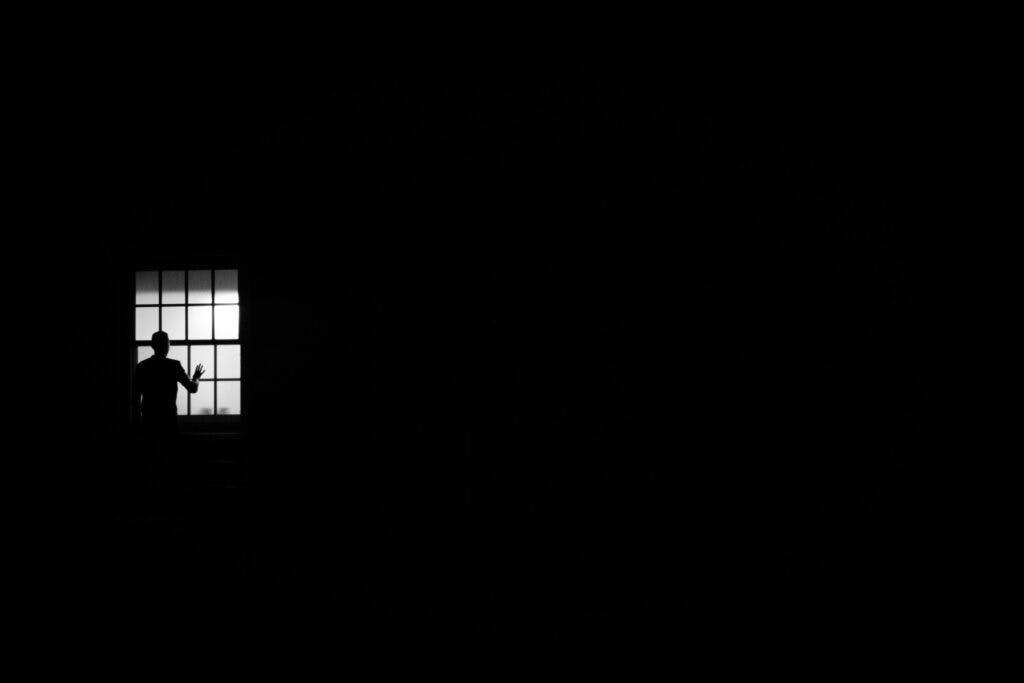 The silhouette of a man looking outside his window in the dark.