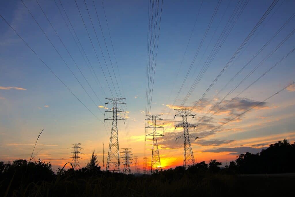 Several towers holding electrical lines with the sun setting in the background.