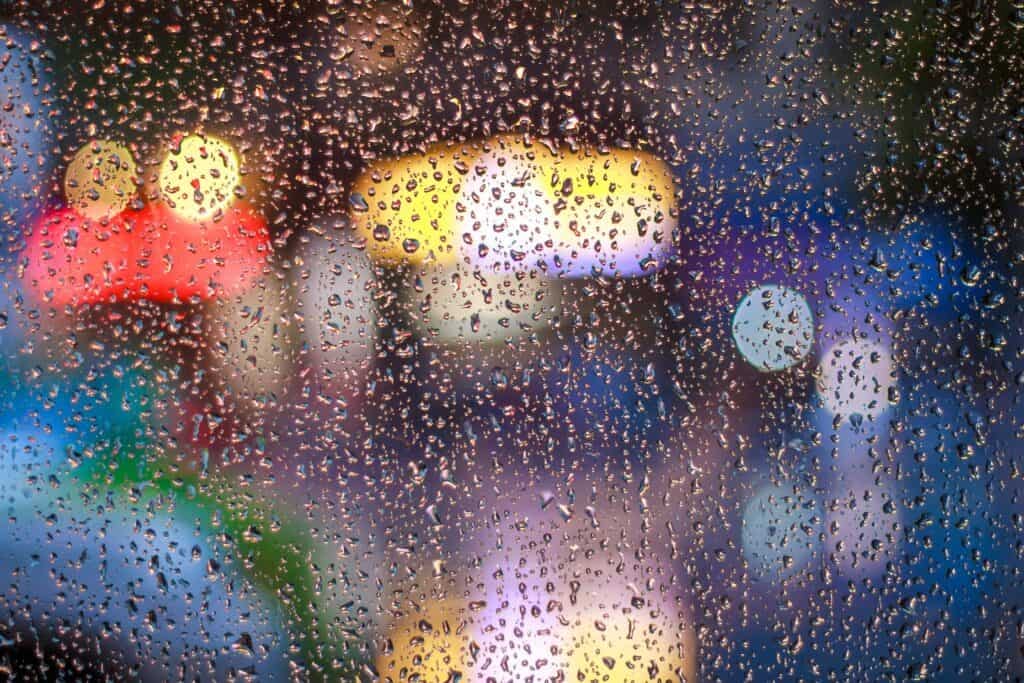 A window with rain on it with blurry lights in the background.