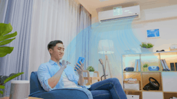 Happy man on smartphone enjoying the smart air conditioner in his living room.