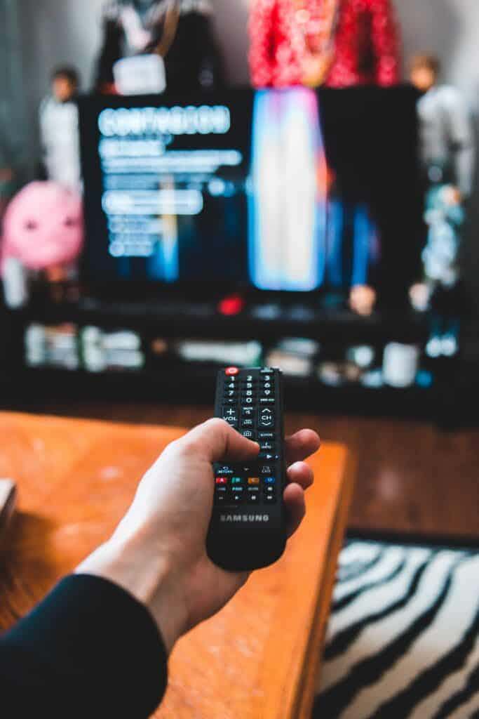 hand holding a remote with tv on in background