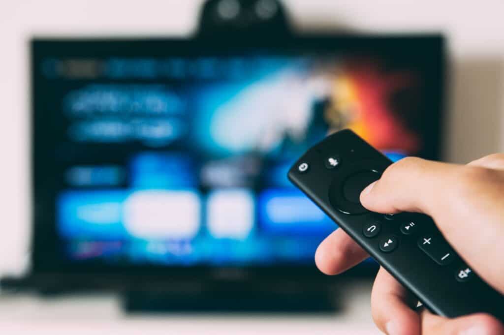 person holding amazon firestick remote with tv in background