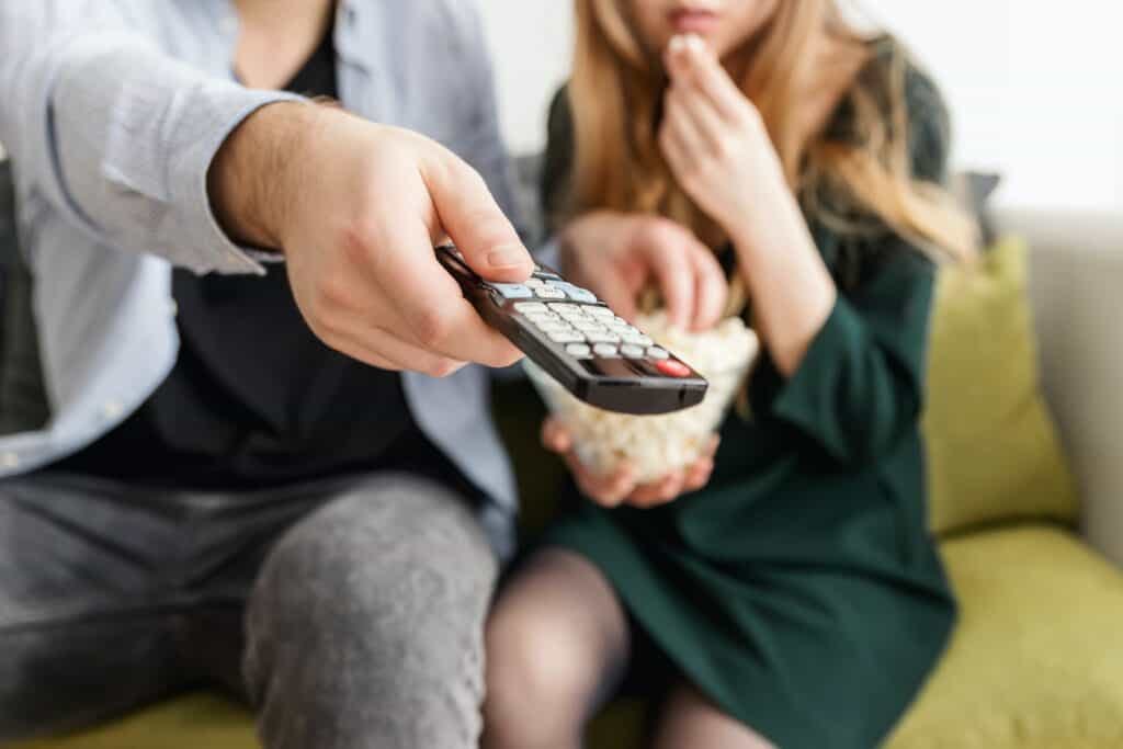 couple eating popcorn on couch changing tv channel with remote in hand