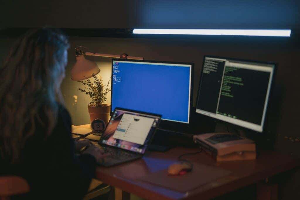women typing on laptop with 2 computer monitors behind her on desk