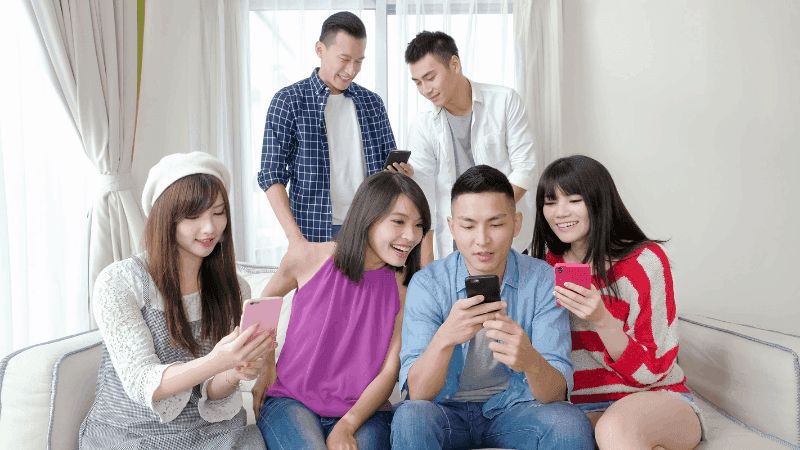 Group of 6 happy people on their smart phones in a living room