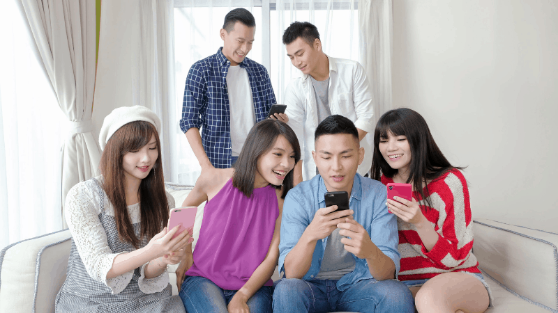 Group of 6 happy people on their smart phones in a living room