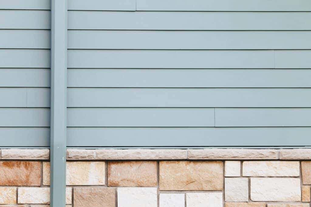 The siding of a light blue house with brick accent.
