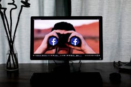 a computer with an image of man holding binoculars with Facebook logo in them