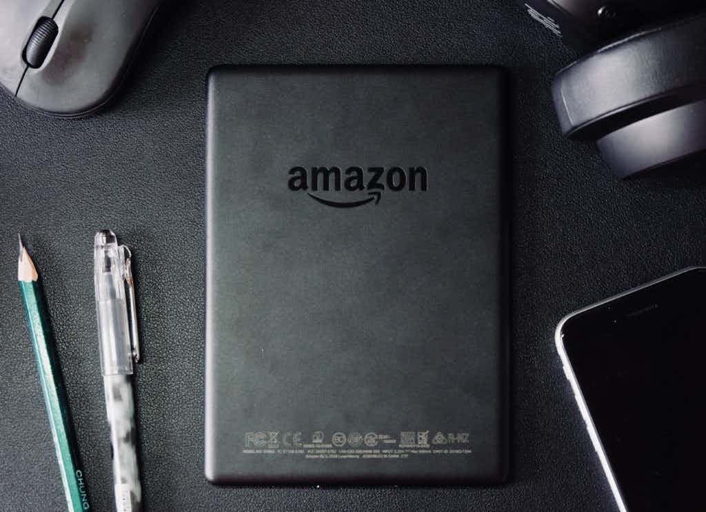 Amazon kindle with pens, a smartphone, mouse, and headphones around it