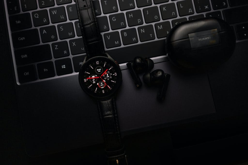 Samsung Galaxy Watch on a black computer with earpods