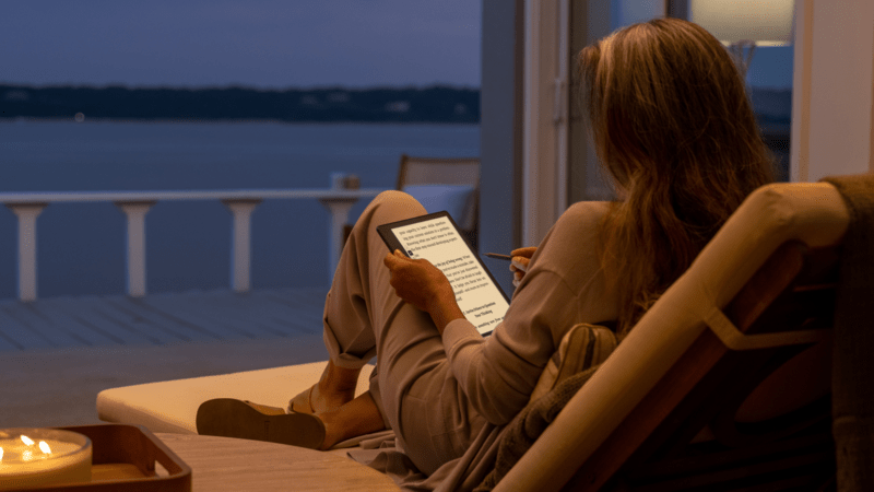 A woman using a Kindle Scribe by the water