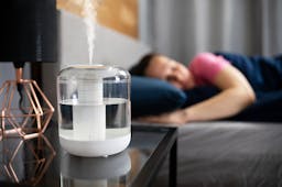 Air humidifier steam on nightstand near young lady sleeping